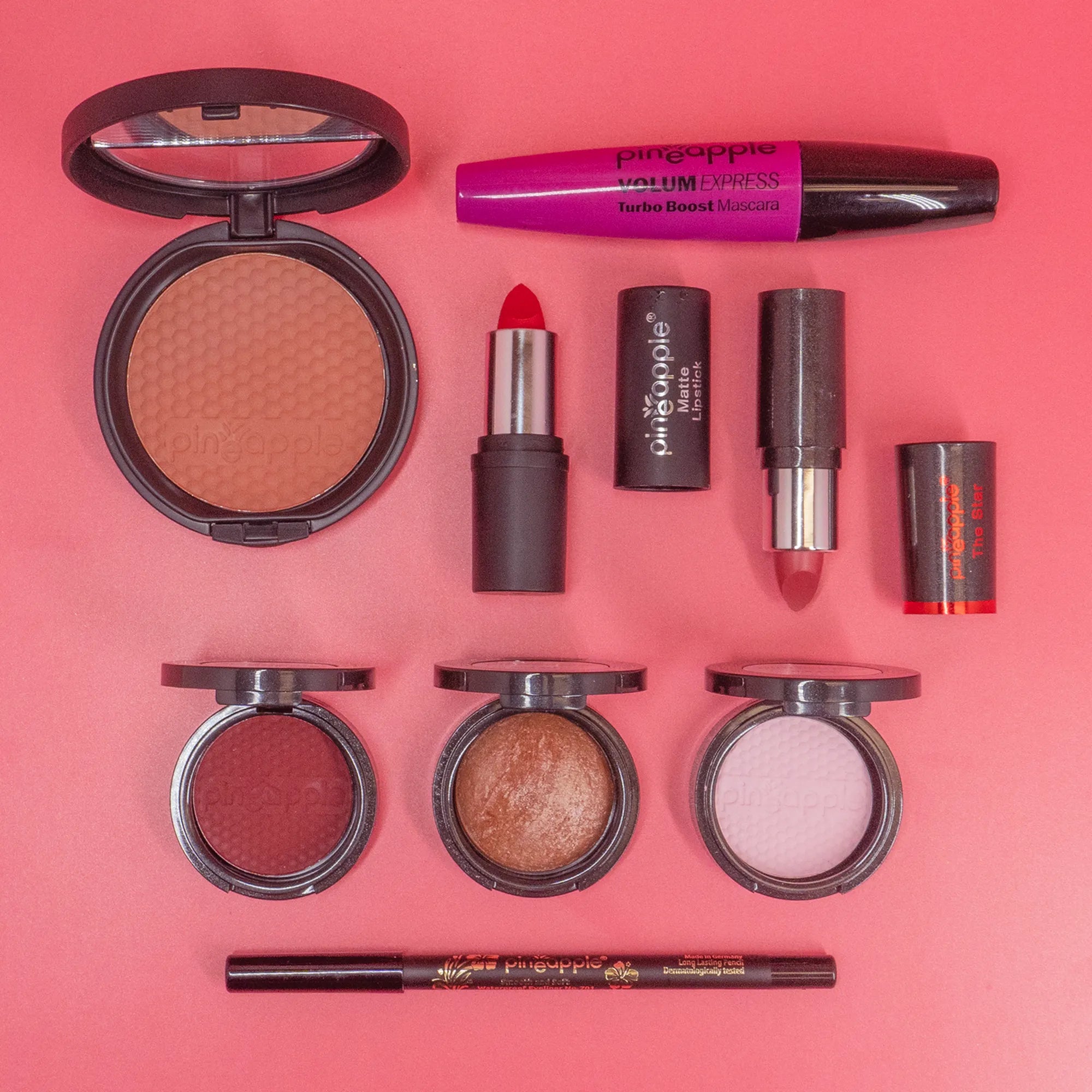 Collection of makeup products including blush, lipstick, and mascara on a pink background